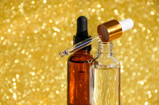 Primo piano del siero in bottiglie di vetro su fondo oro Cosmetici e cura