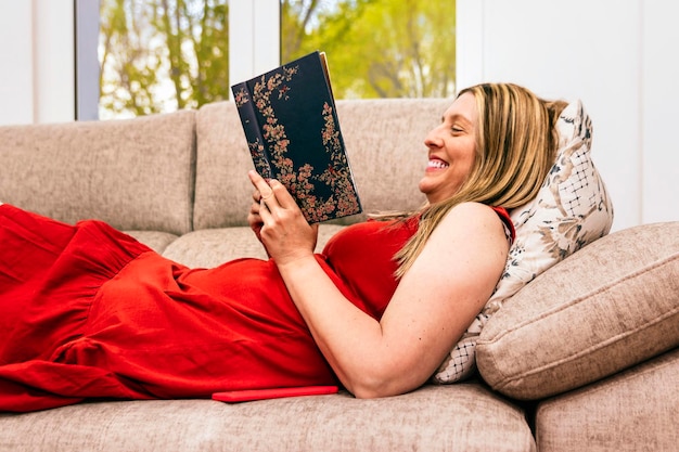 Primo piano del sorriso di una donna che legge un libro sdraiato sul divano di casa