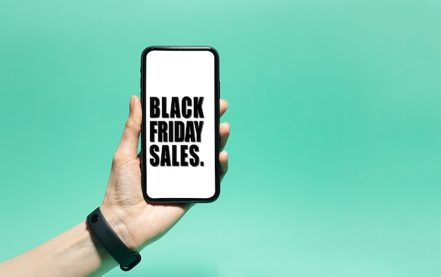 Primo piano del testo di vendita venerdì nero sullo schermo bianco sullo smartphone in mano maschio. Sfondo di colore ciano, aqua menthe.
