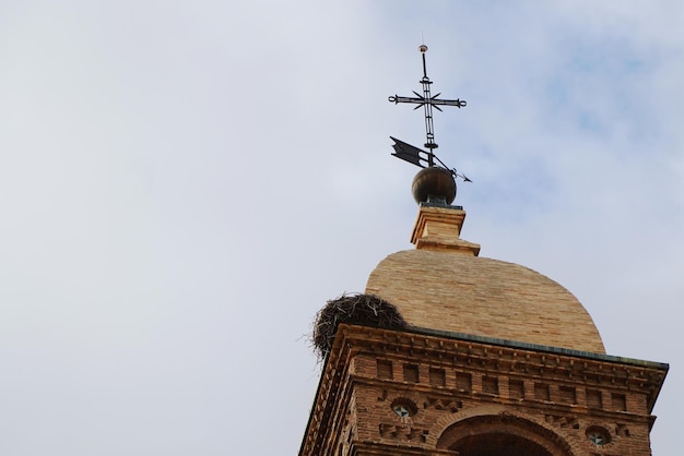 Primo piano del vecchio campanile con croce in acciaio e nido di cicogna