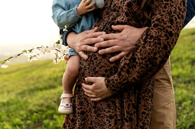 Primo piano del ventre di una donna incinta che è abbracciata dalle braccia del marito cuore sul ventre futuri genitori coppia incinta che cammina nella natura