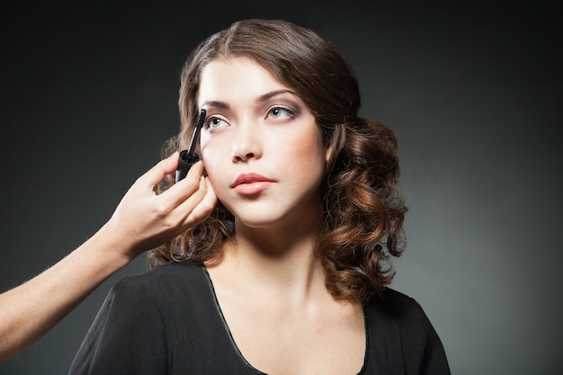 Primo piano del viso di donna con pennello mascara su sfondo scuro