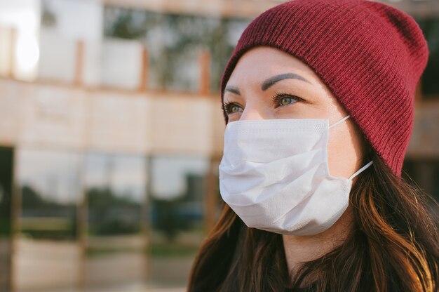 Primo piano del viso di una ragazza in una maschera medica. Sullo sfondo di un business center in vetro.