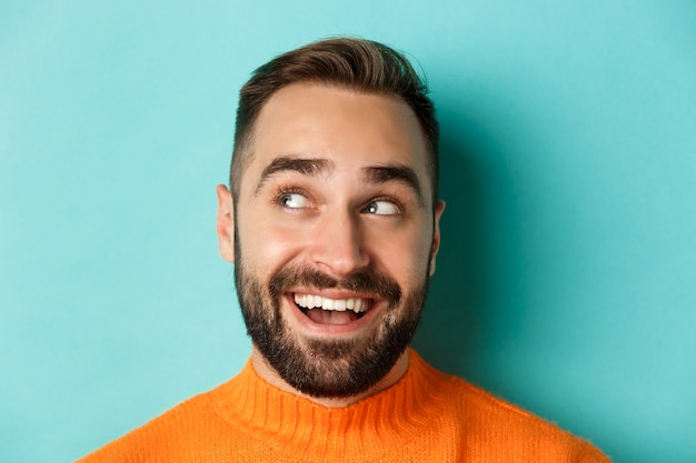 Primo piano del volto dell'uomo caucasico bello guardando il logo nell'angolo in alto a sinistra e sorridendo soddisfatto, controllando l'offerta promozionale, in piedi su sfondo turchese.