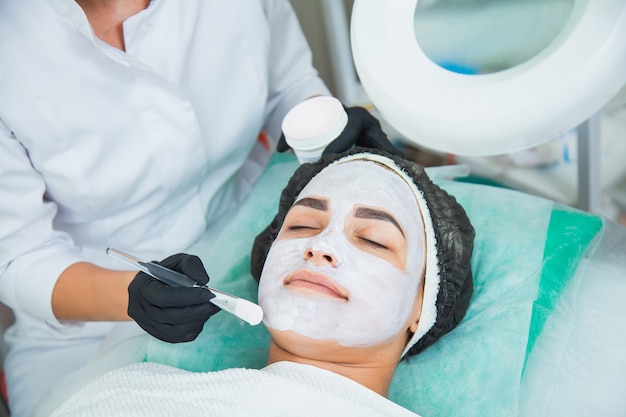 Primo piano del volto di donna nella procedura di maschera di argilla bianca nel salone di bellezza. Maschera peeling viso, trattamento di bellezza spa, concetto di cura della pelle.