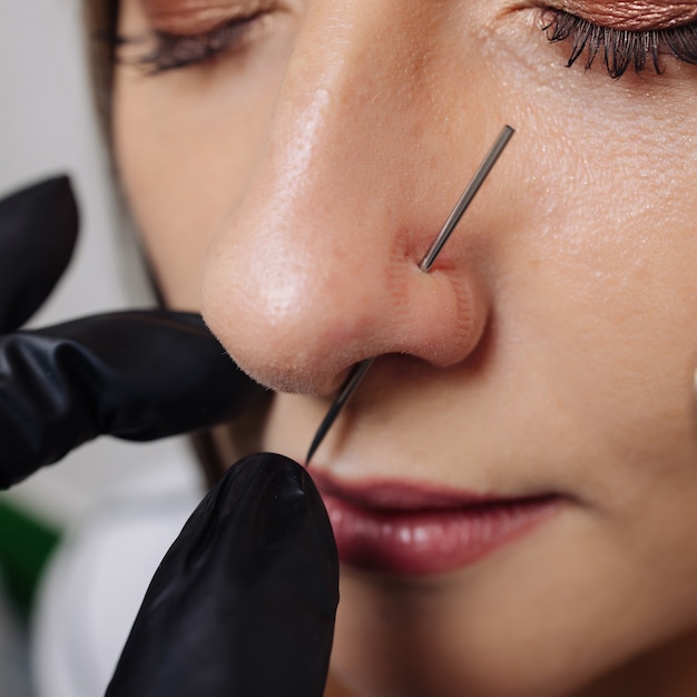 Primo piano del volto di una giovane donna con piercing appeso al naso.