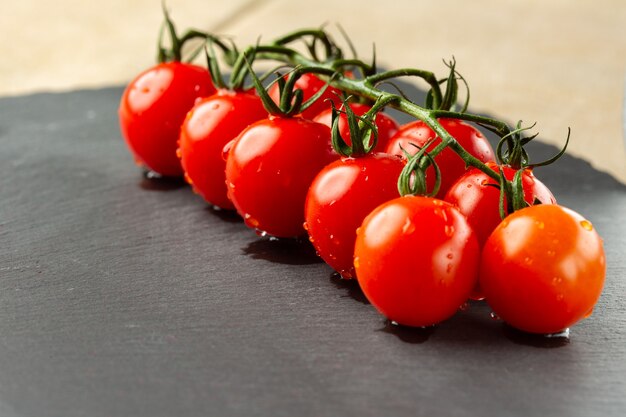 Primo piano dell'ardesia nera con un ramo di un ramo di pomodoro ciliegino maturo bagnato su di esso