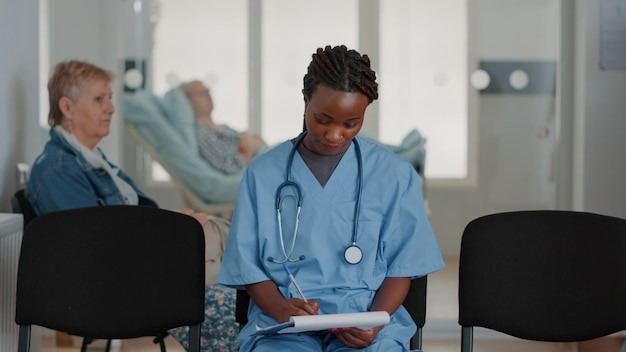 Primo piano dell'assistente medico che analizza i fogli degli appunti nell'area di attesa, preparandosi per la consultazione di controllo per il trattamento della malattia. Infermiera donna che esamina i documenti sanitari nella lobby.