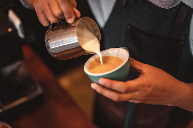 Primo piano dell'estrazione professionale del caffè da parte del barista con un versamento di latte cotto a vapore nella tazza da caffè che produce una bella arte del latte. caffè, estrazione, profondità, tazza, arte, concetto di barista.