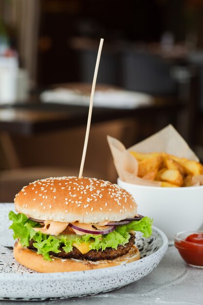 Primo piano dell'hamburger con insalata e salsa sulla tavola di cemento, fondo del ristorante. grande hamburger con patatine fritte e ketchup.