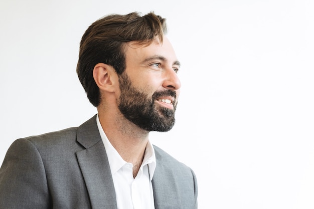 Primo piano dell'immagine di un uomo d'affari di successo con la barba che indossa un abito formale che sorride e guarda da parte mentre lavora in ufficio
