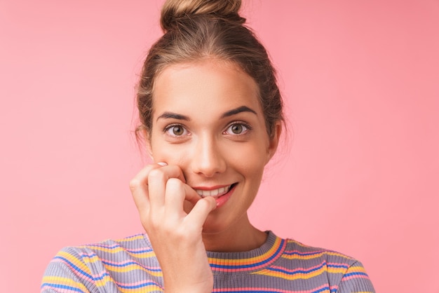 Primo piano dell'immagine di una bella donna adorabile che indossa abiti casual che sorride e si morde le unghie isolate su un muro rosa