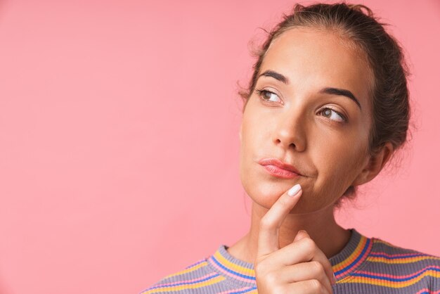 Primo piano dell'immagine di una bella donna attraente vestita con abiti colorati che pensa e guarda da parte il copyspace isolato su una parete rosa