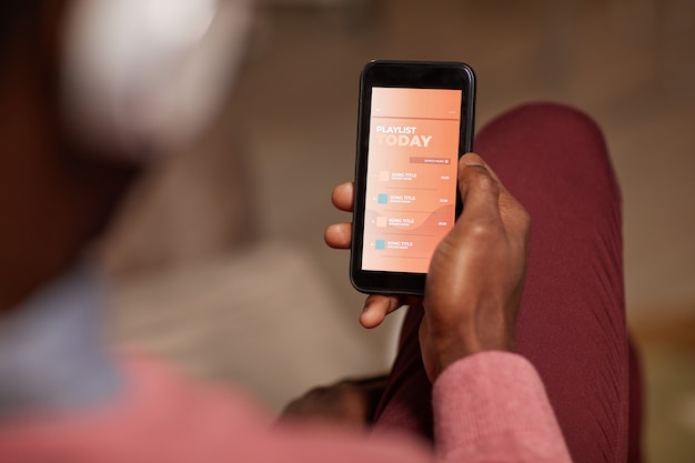 Primo piano dell'uomo africano che tiene il suo telefono cellulare e gode della sua playlist del giorno