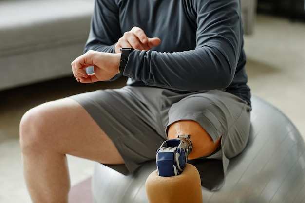 Primo piano dell'uomo con la gamba protesica che controlla lo smartwatch durante lo spazio della copia dell'allenamento