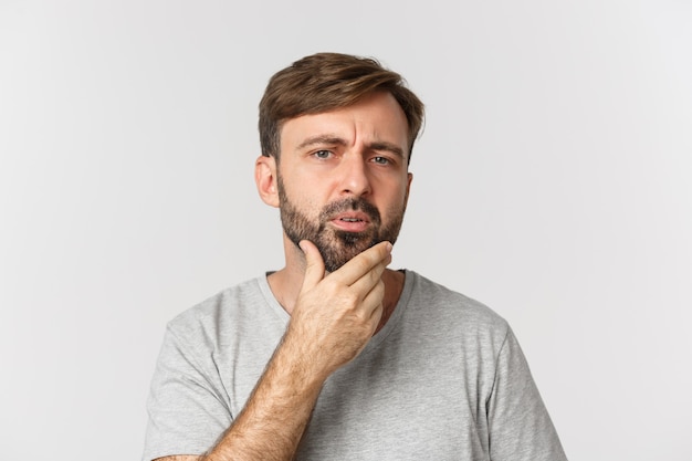 Primo piano dell'uomo confuso che tocca la sua barba e che guarda se stesso