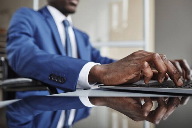 Primo piano dell'uomo d'affari africano che digita sulla tastiera sul computer portatile al tavolo