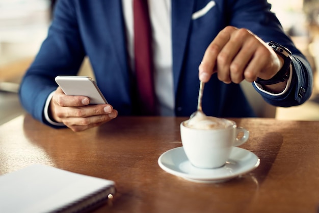 Primo piano dell'uomo d'affari che beve una tazza di caffè mentre utilizza lo smartphone in un caffè