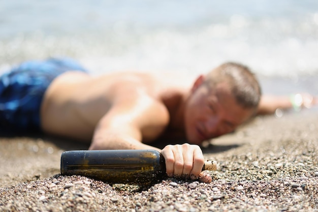 Primo piano dell'uomo dunk sdraiato in riva al mare con una bottiglia di vino in mano incidente in mare annegamento di