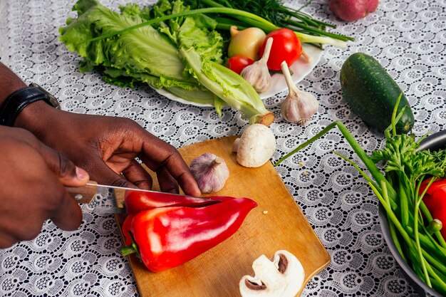 Primo piano dell'uomo mani afroamericano tagli verdure friggere insalata pepe, funghi, pomodoro in cucina ricettario sul tavolo .vegan cibo sano.