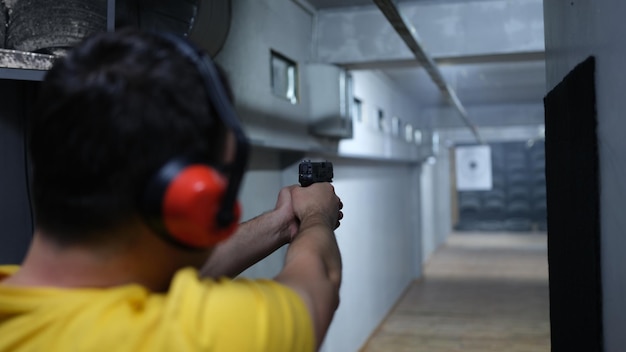 Primo piano dell'uomo sparatutto in cuffia che spara al tiro al bersaglio praticando con la pistola nel fucile