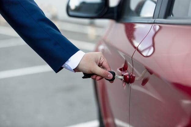 Primo piano dell'uomo vestito che apre la portiera dell'auto con la chiave