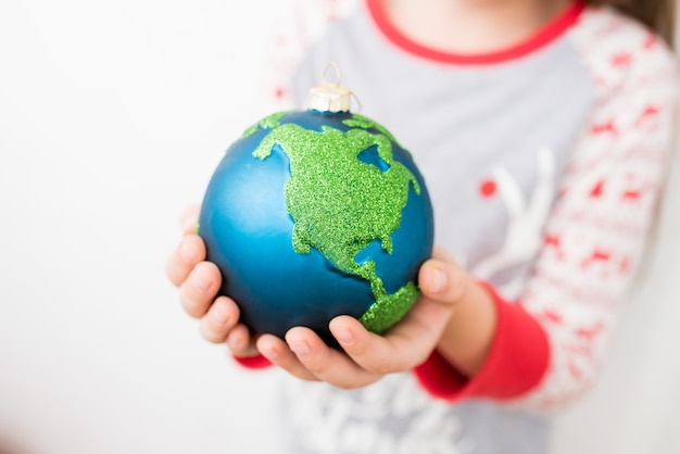 Primo piano della bambina che tiene in mano la pallina di vetro di Natale decorazione ornamento globo pianeta terra