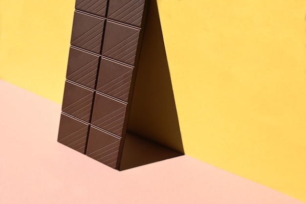 Primo piano della barretta di cioccolato con ombre su sfondo giallo e rosa, concettuale