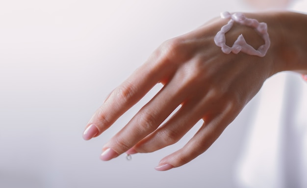 Primo piano della bella mano della donna con le dita lunghe che applicano crema idratante e lenitiva sulla pelle
