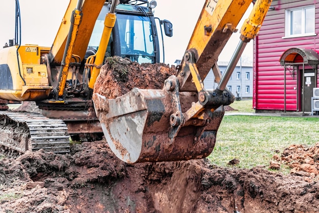 Primo piano della benna dell'escavatore in cantiere. L'escavatore sta scavando una trincea per i servizi sotterranei. Macchine edili per lavori di sterro.