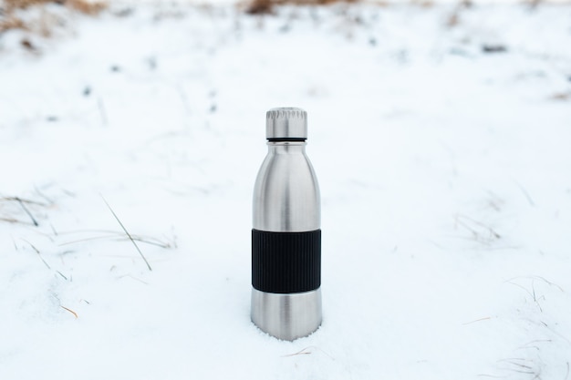 Primo piano della bottiglia d'acqua termo riutilizzabile in acciaio nella neve. Sfondo invernale naturale.