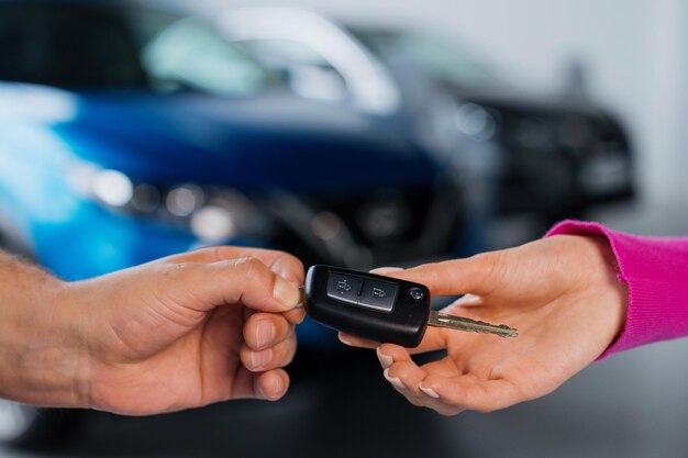 Primo piano della chiave dell'auto che il manager consegna alla giovane donna all'acquirente sullo sfondo dello showroom del centro auto