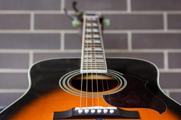 Primo piano della chitarra acustica sopra il fondo del muro di mattoni Concentrarsi sulla buca sonora e sulle corde Industria musicale