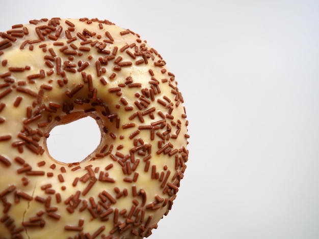 Primo piano della ciambella su sfondo bianco Deliziosa torta ricoperta di glassa alla vaniglia e granelli di cioccolato Colazione o spuntino ad alto contenuto calorico Dessert dolce con ciambella o pasta al cioccolato e vaniglia