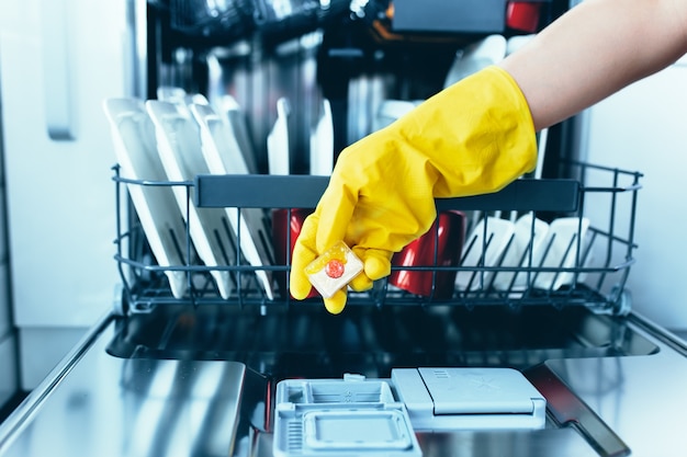 Primo piano della compressa di sapone per lavastoviglie che tiene la mano della donna.