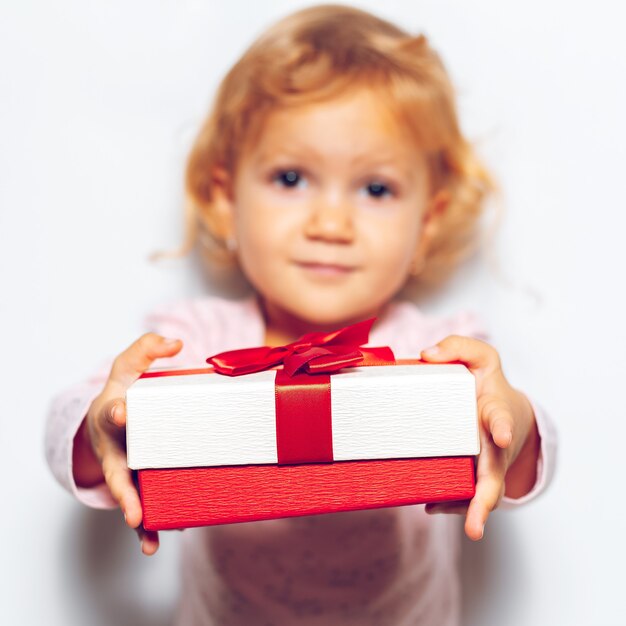 Primo piano della confezione regalo con fiocco di nastro rosso nelle mani della ragazza dei bambini.