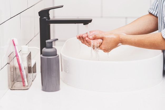 Primo piano della donna asiatica che si lava con l'acqua del rubinetto nel bagno di casa