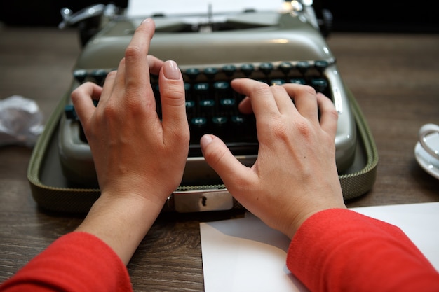 primo piano della donna che digita sulla vecchia macchina da scrivere a tavola