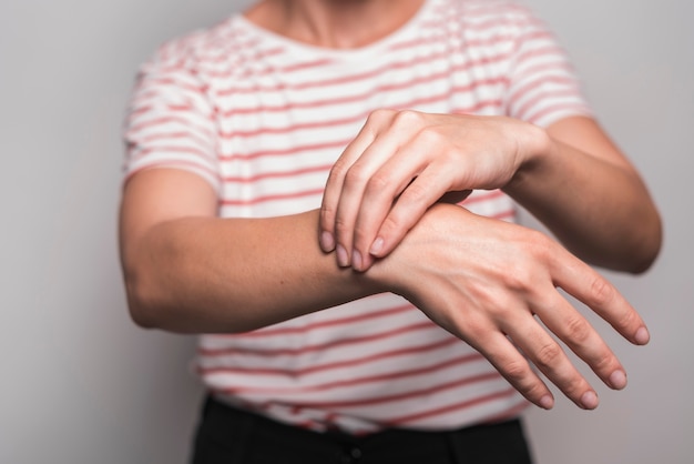 Primo piano della donna che ha dolore al polso che sta contro il fondo grigio