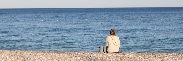 Primo piano della donna che si siede sulla spiaggia di ciottoli vicino al mare pittoresca spiaggia femminile godendo e