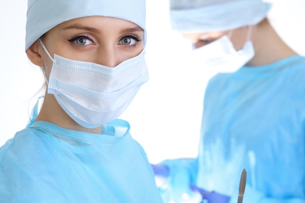 Primo piano della donna chirurgo che guarda la fotocamera mentre i colleghi si esibiscono in background nella sala operatoria isolata