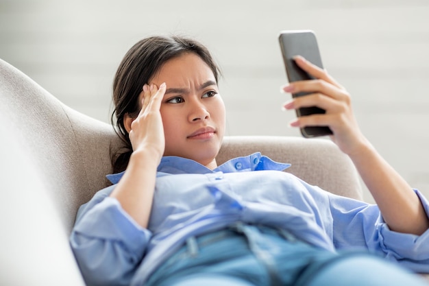 Primo piano della donna cinese che soffre di mal di testa utilizzando lo smartphone
