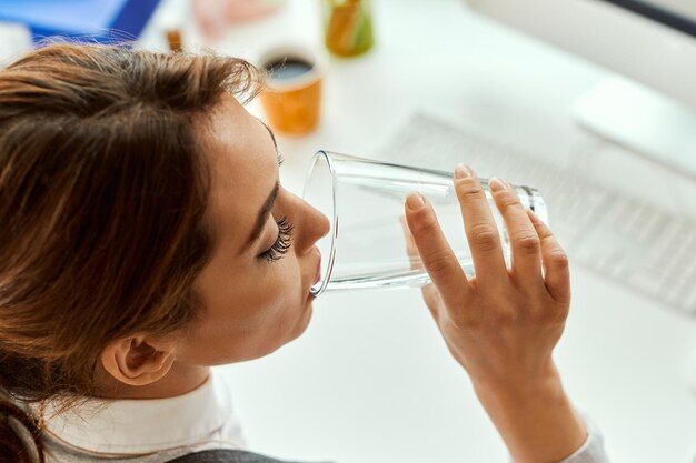 Primo piano della donna di affari che beve un bicchiere d'acqua in ufficio