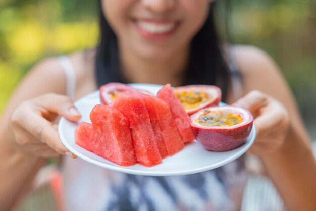 Primo piano della donna ha sollevato un piatto di frutta con anguria e frutto della passione Ragazza goditi la frutta a pranzo concetto di dieta di benessere Concetto di salute