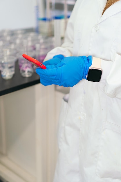 Primo piano della donna in camice utilizzando il telefono in laboratorio