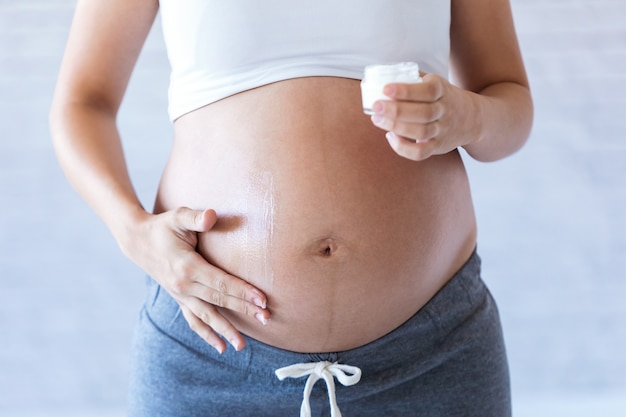 Primo piano della donna incinta che applica la lozione crema per la cura della pelle sulla pancia incinta per prevenire le smagliature.