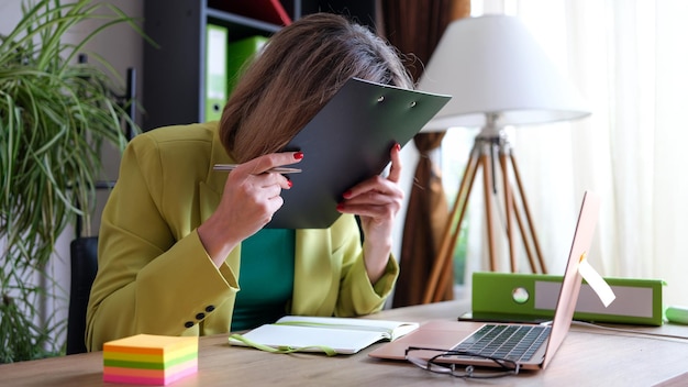 Primo piano della donna sconvolta e oberata di lavoro che copre il viso con il manager dell'ufficio frustrato per appunti