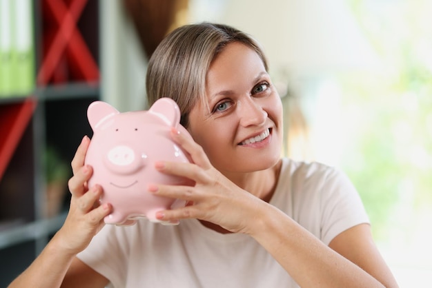 Primo piano della donna sorridente che tiene il porcellino salvadanaio rosa nel concetto bancario e di risparmio delle mani