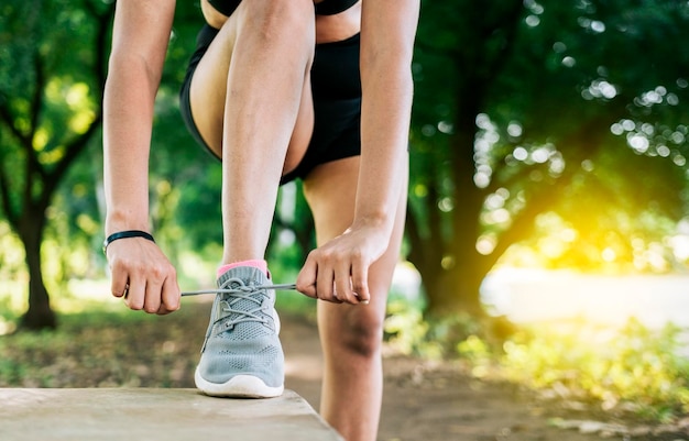 Primo piano della donna sportiva che lega le sue scarpe Ragazza atletica che lega i suoi lacci delle scarpe in un parco Ragazza del corridore che lega le sue scarpe da corsa in un parco con lo spazio della copia