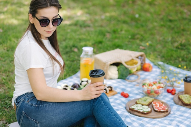 Primo piano della donna tenere una tazza usa e getta con caffè durante il picnic all'aperto Spazio per il testo Concetto di picnic vegano